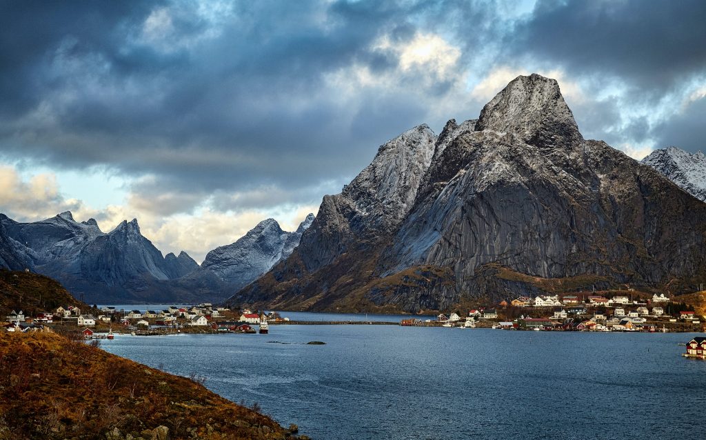 Eine norwegische Landschaft mit kantigen Bergen und einem Dorf, das sich an den Ufern eines Fjords erstreckt.