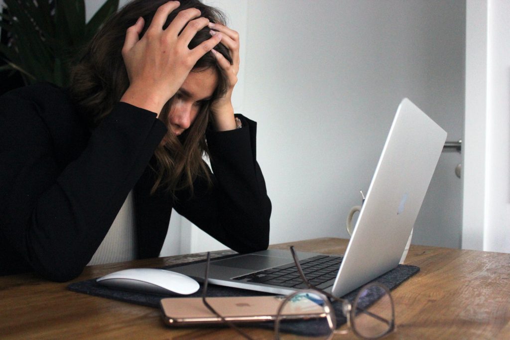 Eine Frau hält sich verzweifelt beide Hände an den Kopf und starrt auf ihr Laptop.