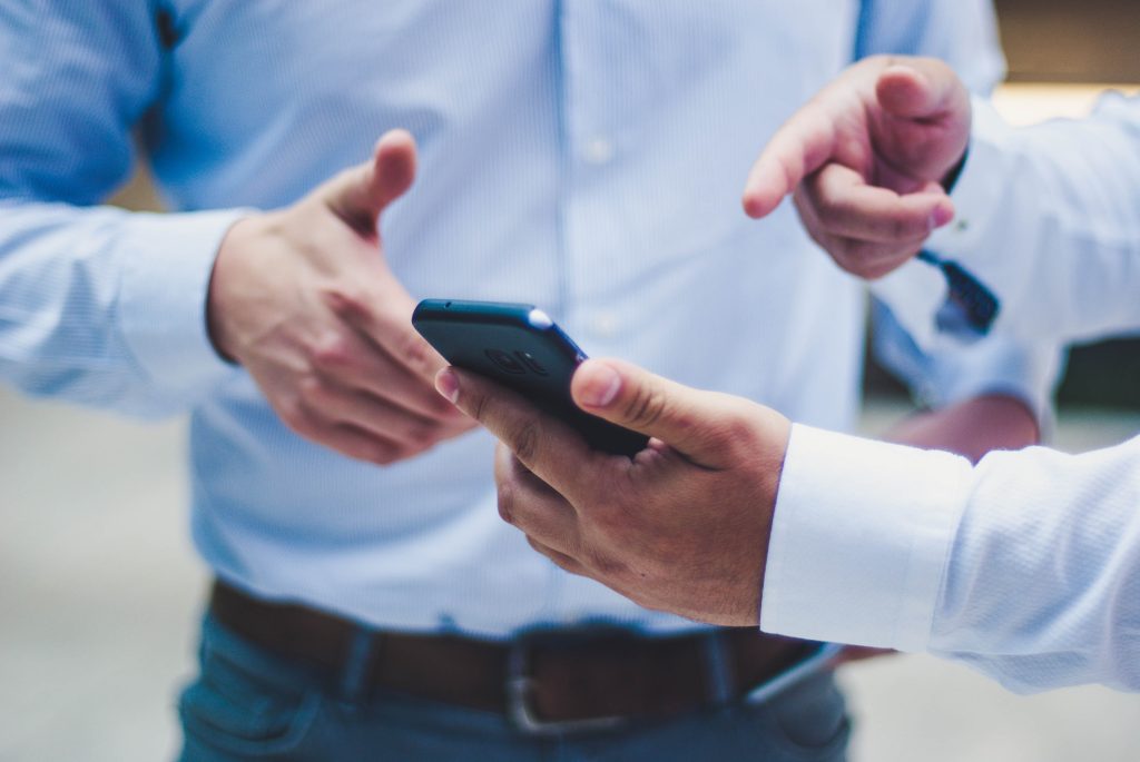 Zwei Männer diskutieren mit den Händen über etwas, das sie auf einem Smartphone sehen.